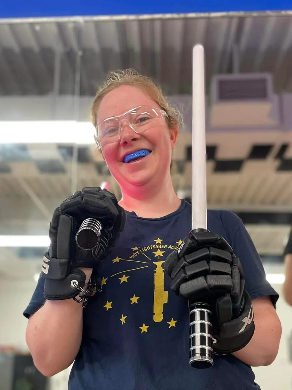 Jennifer Campbell wearing protective glasses and gloves, holding two lightsabers.