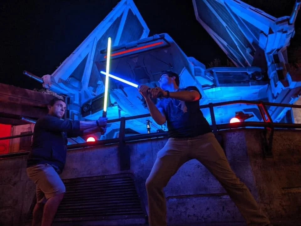 Two people holding illuminated sabers in a training stance.